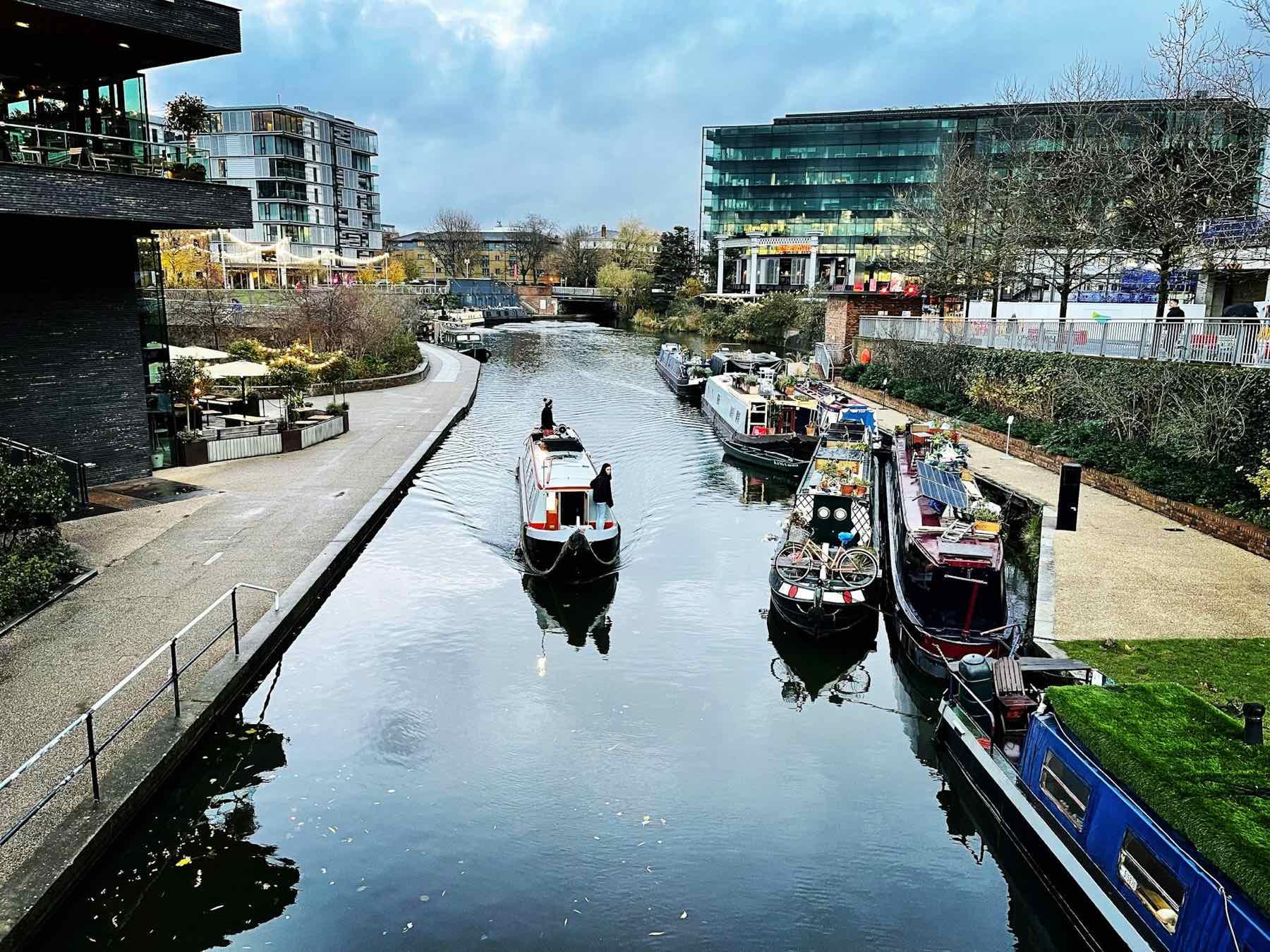 Liveaboard narrowboats moored along a canal in London, with one boat underway